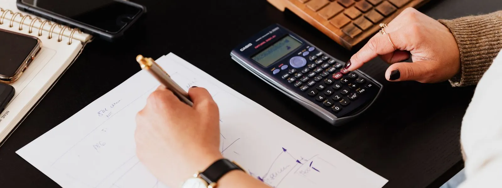 Mãos de contador com calculadora, anotações e documentos sobre a mesa