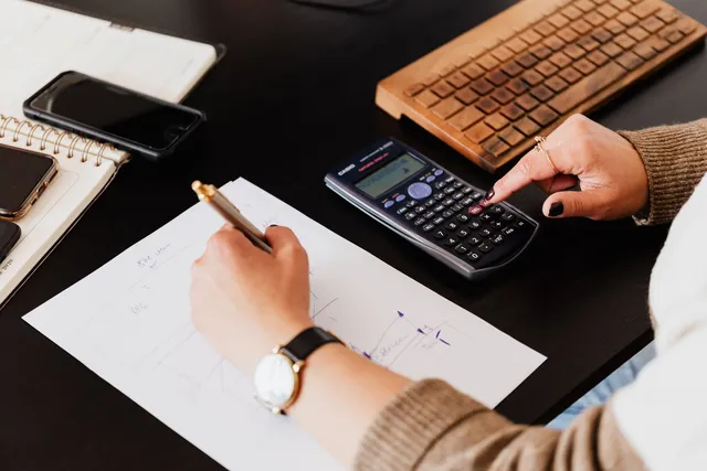 Mãos de contador com calculadora, anotações e documentos sobre a mesa