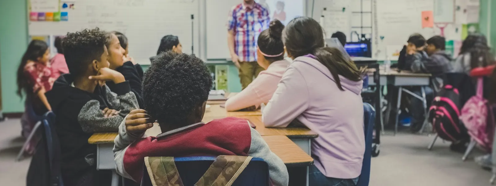 Classroom with students and a teacher at a whiteboard with digital projector